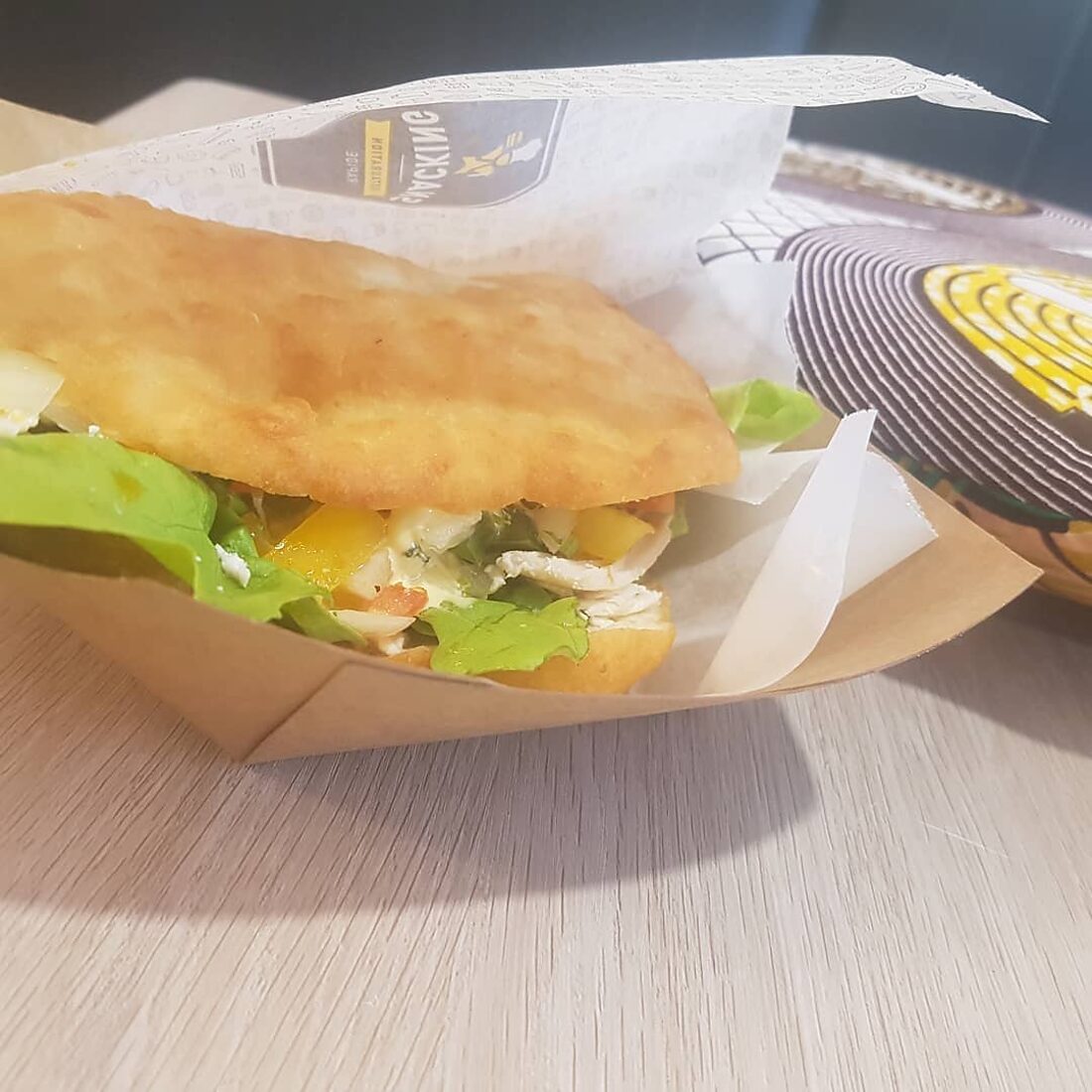Un bokit ouvert et garni de poulet et de crudités, dans son emballage kraft