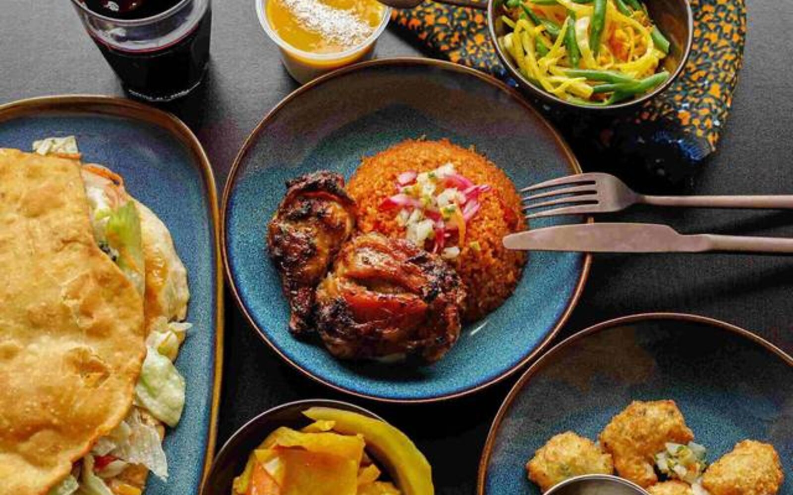 Une tablée : bokit garni, bol de riz rouge au poulet grillé, accras, alocco et bissap